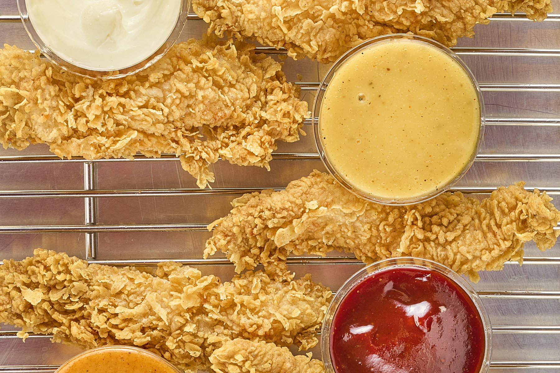 Crispy chicken tenders on a wire rack surrounded by house dipping sauces
